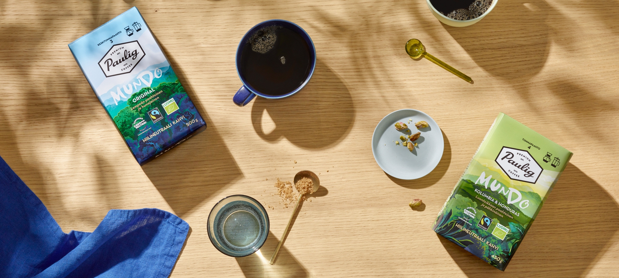 Paulig Mundo -kahvipakkaukset pöydällä hunajan ja lusikoiden kanssa.
